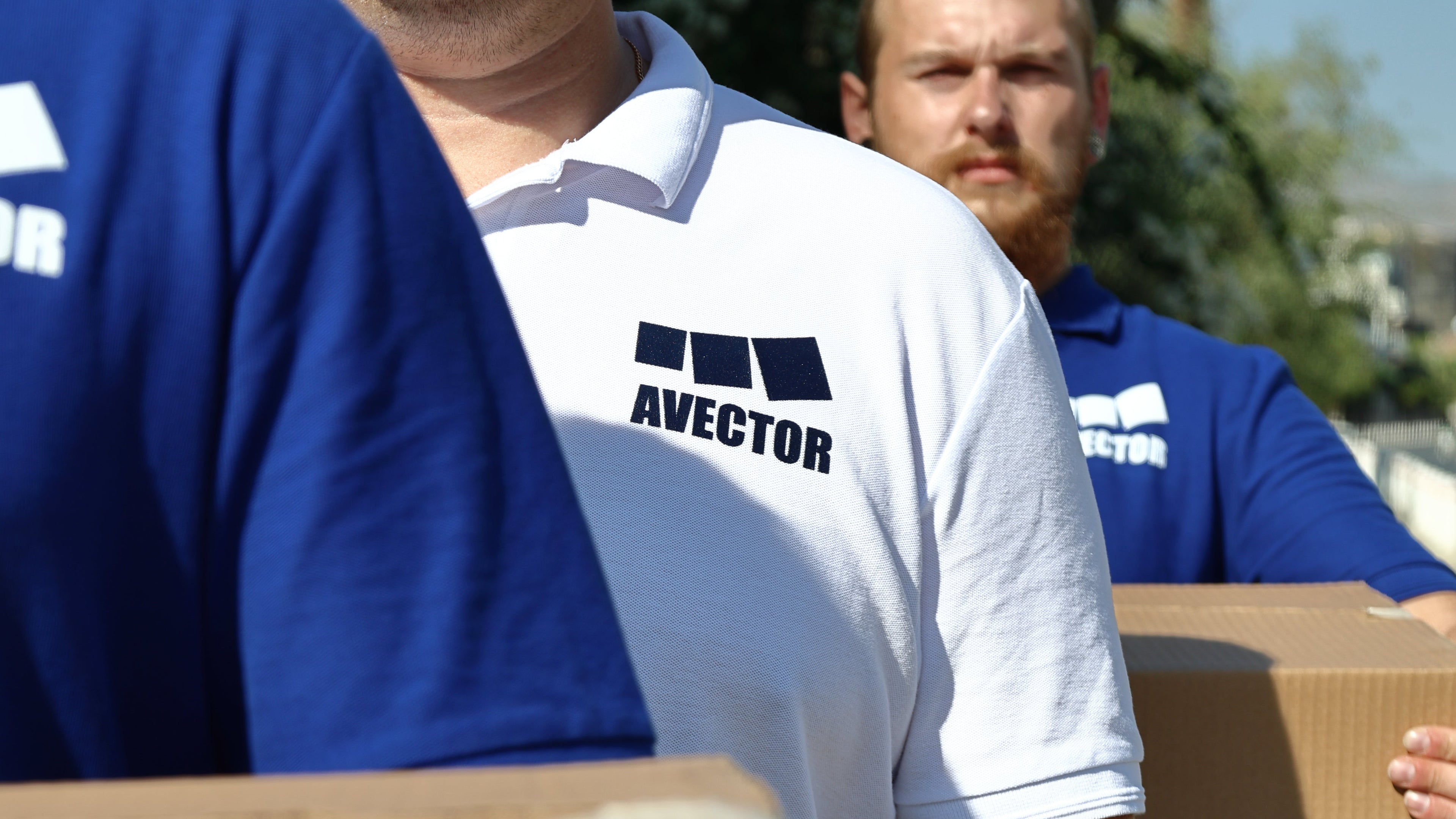 Three men in shirts with the Avector logo carrying boxes