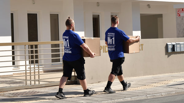Two movers in blue shirts carrying boxes outside a building.