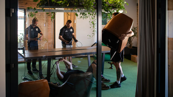 Two people working on a project in a room with green flooring and wooden furniture.
