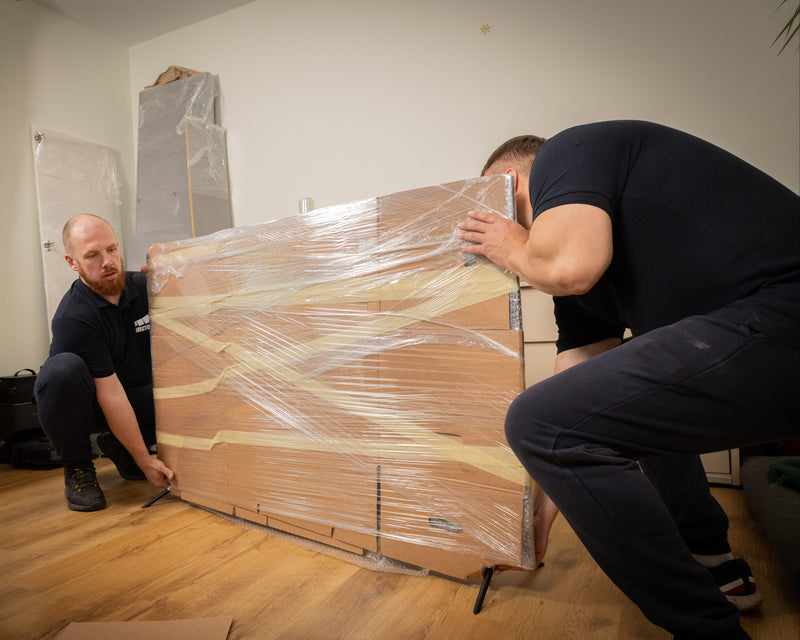 Two Avector workers picking up a packaged TV